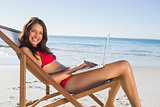 Smiling woman using her laptop while relaxing on her deck chair