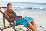 Handsome man using his laptop while relaxing on his deck chair