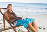 Smiling handsome man using his laptop while relaxing on his deck chair