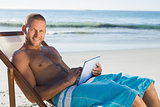 Smiling handsome man using his tablet while sunbathing