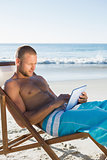 Concentrated handsome man using his tablet while sunbathing