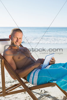 Cheerful handsome man using his tablet while sunbathing