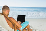 Handsome man typing on his laptop while sitting on his deck chair
