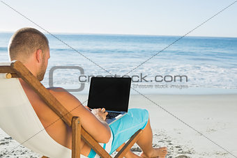 Handsome man typing on his laptop while sitting on his deck chair