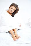 Brunette girl sitting on bed wrapped in quilt