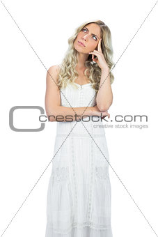 Pensive attractive model in white dress posing touching her head