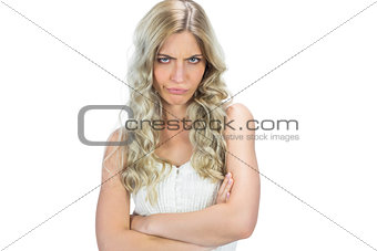 Frowning seductive model in white dress posing crossing arms