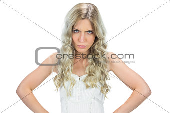 Frowning seductive model in white dress hands on hips