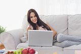 Attractive brunette lying on couch with laptop