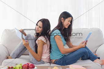 Friends sitting back to back using their tablets