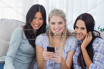 Smiling friends holding smartphone looking at camera