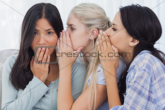 Two friends whispering secrets to surprised brunette