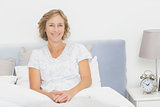 Blonde woman sitting in bed smiling at camera