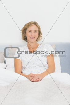 Blonde happy woman sitting in bed smiling at camera