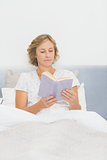 Blonde woman sitting in bed reading