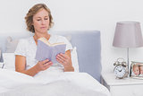 Relaxed blonde woman sitting in bed reading