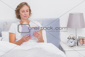 Relaxed blonde woman sitting in bed reading