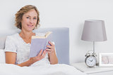 Happy blonde woman sitting in bed holding book