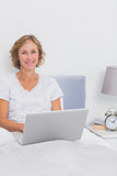 Smiling blonde woman sitting in bed using laptop