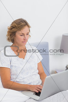 Blonde woman sitting in bed using laptop