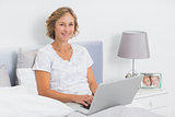 Content blonde woman sitting in bed using laptop