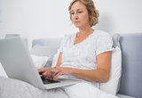 Blonde woman sitting in bed using laptop