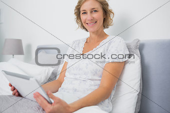 Blonde woman sitting in bed using tablet pc