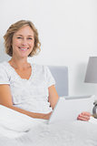 Smiling blonde woman sitting in bed using tablet pc