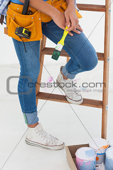 Woman holding paintbrush and wearing tool belt
