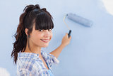 Pretty woman painting wall blue and smiling at camera