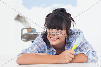Smiling woman lying on floor holding paint brush
