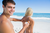 Man putting sun cream on girlfriends back smiling at camera