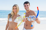 Attractive couple showing snorkels and goggles to camera