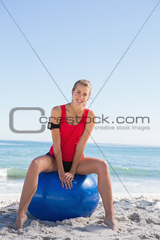 Fit blonde sitting on exercise ball smiling at camera