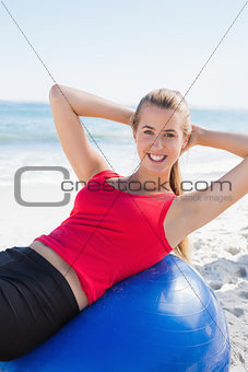 Fit blonde doing sit ups on exercise ball smiling at camera