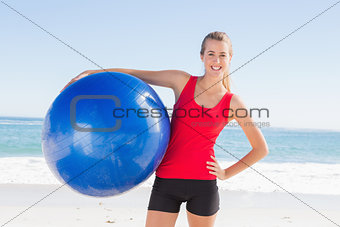 Fit blonde holding exercise ball smiling at camera