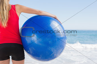 Fit blonde holding exercise ball looking at waves