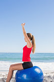 Fit woman sitting on exercise ball stretching arms