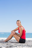 Athletic blonde sitting on sand smiling at camera