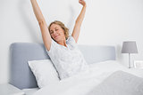 Blonde woman stretching and smiling in bed in the morning