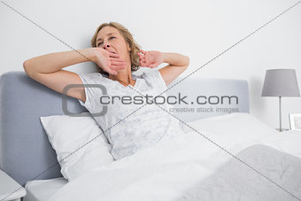 Blonde woman yawning and stretching in bed in the morning