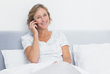 Blonde woman on the phone in bed smiling at camera