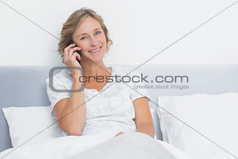 Blonde woman on the phone in bed smiling at camera