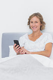 Happy blonde woman sending text message in bed