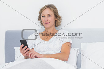 Cheerful blonde woman sending text message in bed