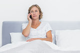Serious blonde woman making phone call in bed