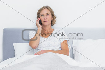 Serious blonde woman making phone call in bed