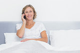 Smiling blonde woman making phone call in bed