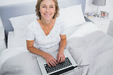 Smiling blonde woman in bed using her laptop