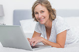 Smiling blonde woman lying on bed using laptop